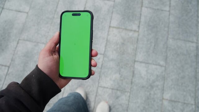 A man casually walks along the street, holding his smartphone up. The close-up reveals the sleek gadget as he interacts with it, embodying the essence of modern technology