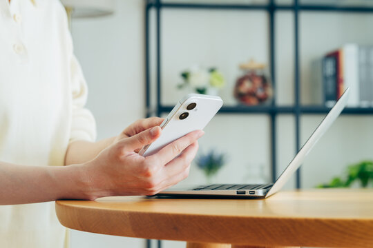家でスマホを持ってパソコンを使う若い女性の手元