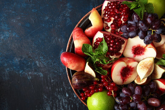 Colorful dish with fruits and berries on platter. Assorted fruits on plate. Pomegranates, figs, peaches, grapes and other fruits on platter. Red currant and mint pour with fruit. Top view. Copy space