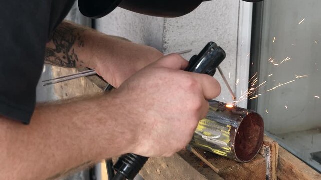 Worker hands with tattoo welding metal pipe during DIY fabrication project