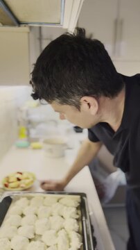 Man leans over baking tray filled with fresh dough pieces on counter. Guy explains recipe holding apple from plate as checks pastry rows slow motion
