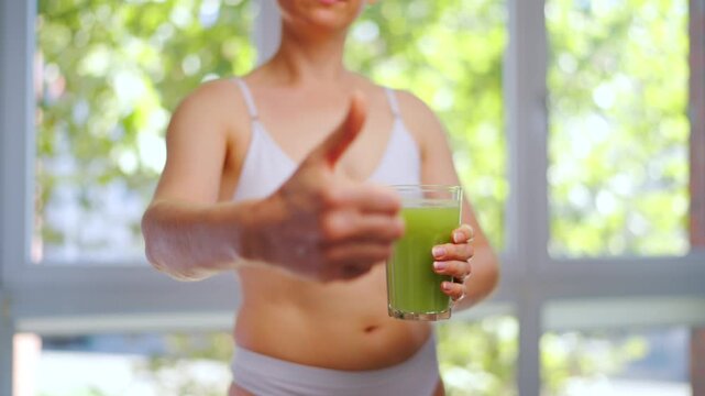 Woman is holding a glass of selery juice in her hand and shows a thumb up.