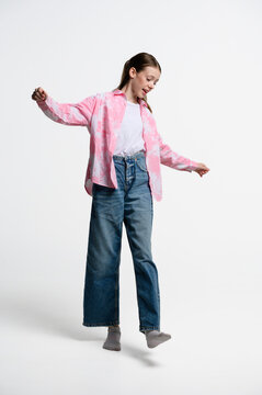 Full length portrait of cheerful teenage girl balancing on one foot. Casual fashion, movement and coordination concept isolated on white studio background.