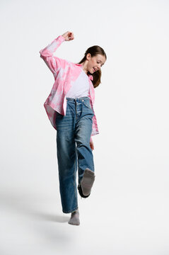 Portrait of playful teenage girl balancing on one foot and kicking leg forward. Casual lifestyle, movement and coordination concept isolated on white background.