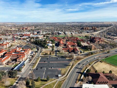 Boulder, USA - 26 December 2025: Aerial view of the University of Colorado Boulder campus with iconic red-tiled roofs, green spaces, and the distant Flatirons under a clear blue sky.