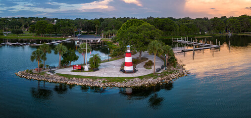 Aerial panorama of Mount Dora Lighthouse on Lake Dora at sunset with boat docks and palm trees in Florida. USA. May 18, 2023.  © JHorsey