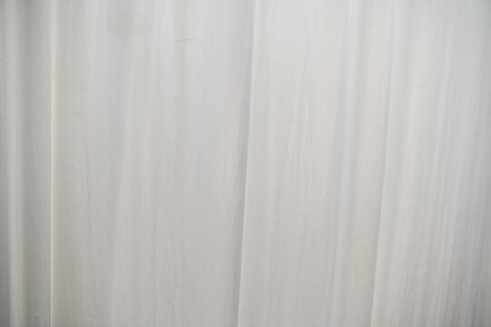 A clean and minimalist texture background showcasing a white, semi-translucent sheer fabric curtain hanging vertically in soft, elegant folds.