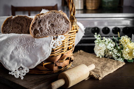 Freshly baked sourdough bread in a rustic basket with a rolling pin and white flowers, showcasing organic ingredients, artisan craftsmanship, premium bakery quality, and cozy kitchen warmth