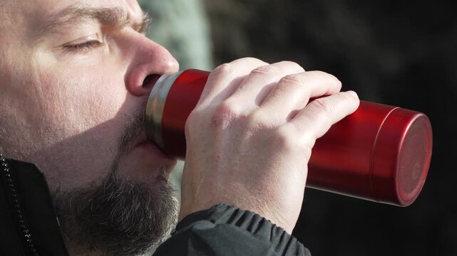 Man Drinking Coffee Adult male in warm clothing drinks hot beverage from red thermos outdoors during a cold winter day
