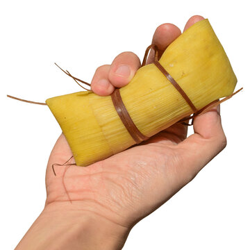 M&atilde;o de homem segurando uma delicia pamonha caseira tradicional enrolada na palha do milho
