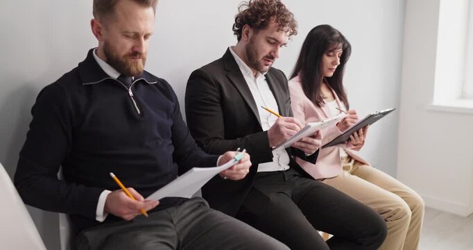 Candidates and applicants waiting for interview and hiring. Three jobseekers fill paperwork on clipboards in a bright lobby, preparing for recruitment by HR. Clear concept of the hiring process.