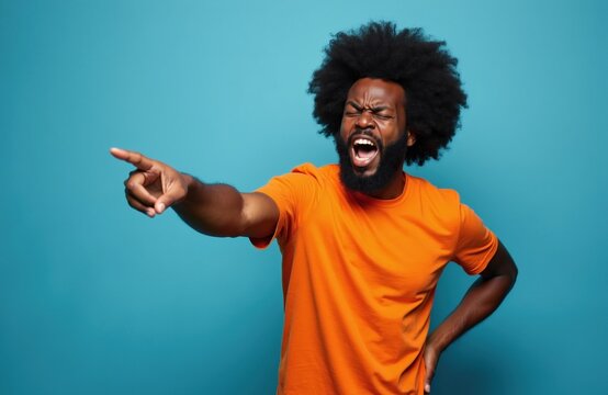 Man with afro hair in orange shirt shouts pointing to side with angry face. He looks upset, giving orders to leave, expressing frustration and discontentment indoors. Isolated studio shot.