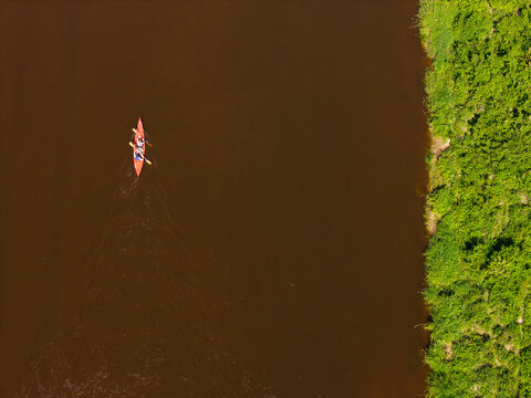 Aerial view of a red canoe with two people paddling on the dark waters of the Gauja River, bordered by lush green forest in Gauja National Park, Incukalns, Sigulda Municipality, Latvia.