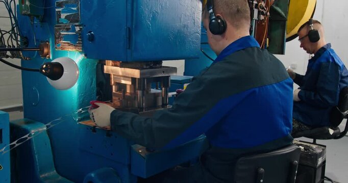 Two machine operators feeding metal strips into stamping presses during industrial production of formed metal parts