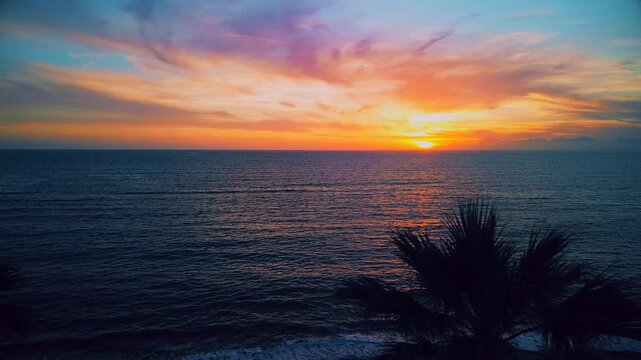 A breathtaking panoramic view of a dramatic golden sunset over the Mediterranean Sea in Agropoli, Cilento coast. The sky is filled with vibrant hues of orange, pink, yellow, and blue clouds, while the