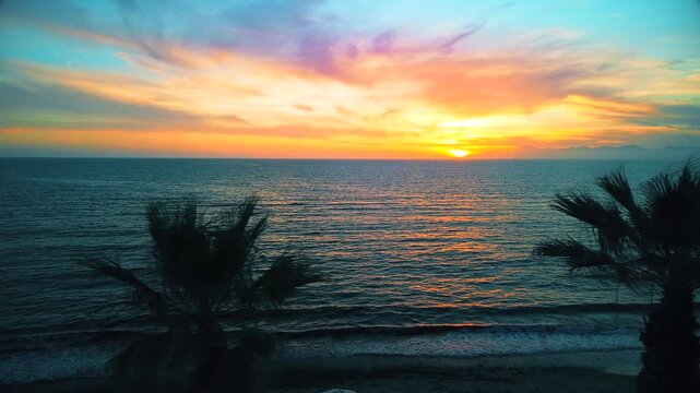 A breathtaking panoramic view of a dramatic golden sunset over the Mediterranean Sea in Agropoli, Cilento coast. The sky is filled with vibrant hues of orange, pink, yellow, and blue clouds, while the