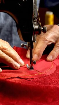 Tailor sewing red fabric with vintage sewing machine close-up.