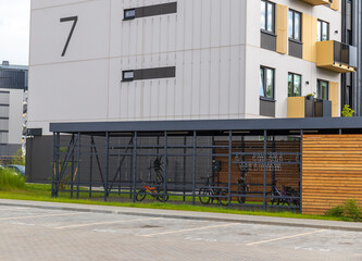 Naklejka premium Modern secure bicycle storage locker and outdoor parking zone next to a contemporary residential apartment building. Urban