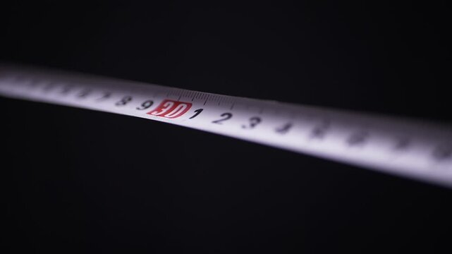 A macro view of a white measuring tape extending diagonally over a solid black background. Concept of precision, accurate dimensions, construction work, and exact measurement.