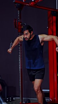 Man athlete gym cable exercise strength training workout muscle fitness machine focused chest fly movement dark indoor background active lifestyle arm muscle black sportswear Vertical