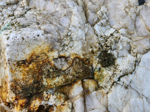 Close-up texture of a rough, weathered quartz rock with mineral inclusions and veins, background, texture