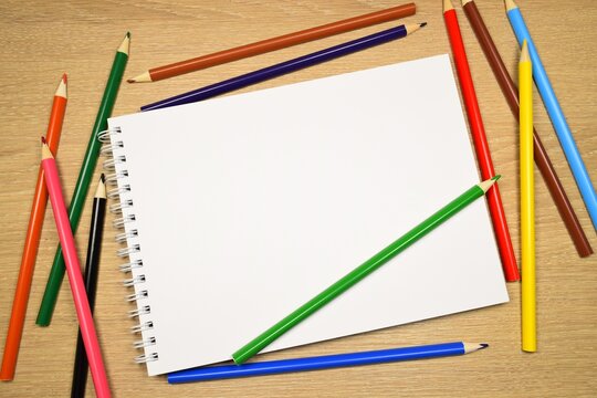 Colored pencils and a notebook on a wooden table