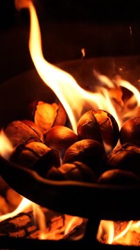 Roasted chestnuts cooking in pan over open fire flames.