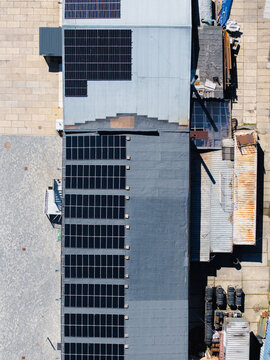 Aerial view of a building roof covered with rows of solar panels, showing the industrial layout and paved ground in Ulbroka, Ropazi Municipality, Latvia.