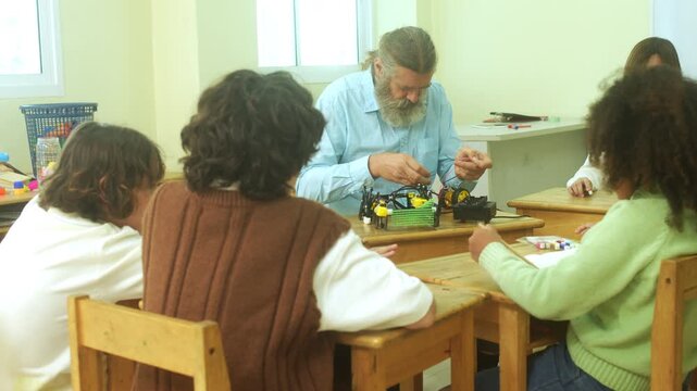 Multi-ethnic elementary school children assembling DIY robotic models during a STEM class with a senior teacher.