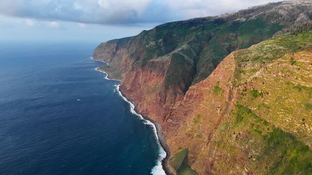 Steep volcanic coastline of Madeira Island filmed from above, showing sharp cliffs meeting the Atlantic Ocean