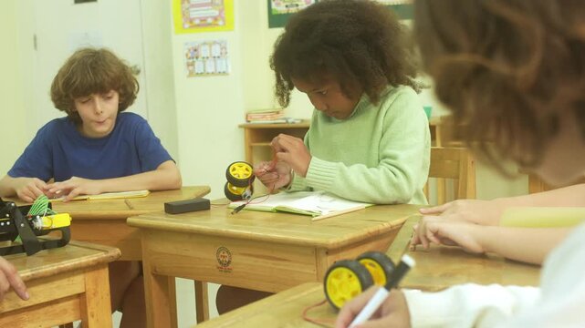 Multi-ethnic elementary school children assembling DIY robotic models during a STEM class with a senior teacher.