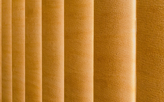 Close-up abstract background of textured orange vertical window blinds, showing repeating parallel slats, fabric patterns, and soft gradient lighting effects