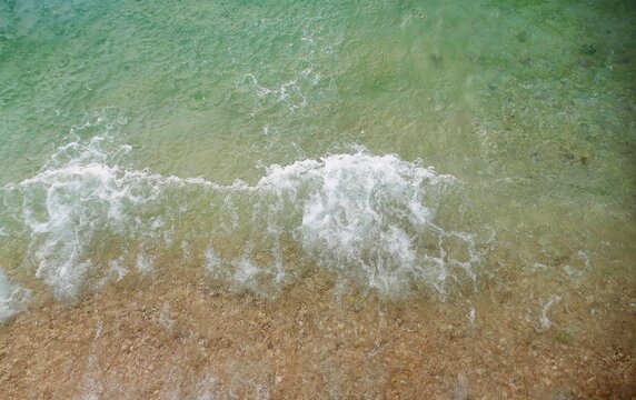 Turquoise sea surface with waves splash on the shore, ariel water splash background