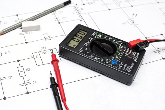 Black digital multimeter with tester probes on electrical drawing