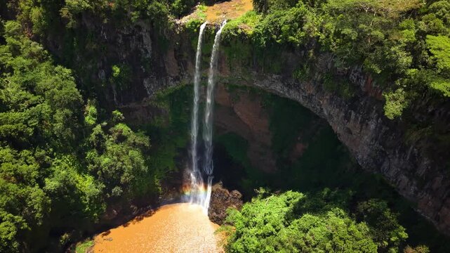 Aerial view of a majestic waterfall cascading into a tropical jungle pool with a rainbow