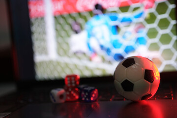 Online soccer gambling and betting. Balls and dice in front of a laptop with live soccer broadcasts. Live scores and results.  © PANCASONA CREATION