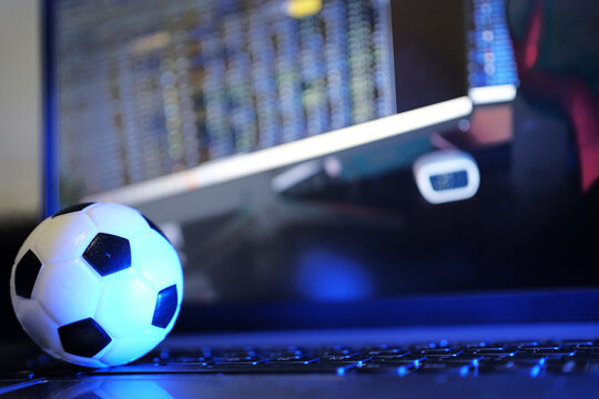 A miniature soccer ball on a keyboard with a football club financial table in the background. A modern football management concept with club data in a computerized system.