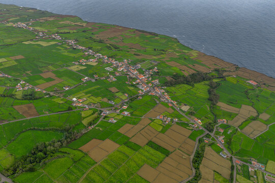 Aerial view of the village of Doze Ribeiras with its characteristic stone walls and lush green fields situated along the Atlantic coastline in Doze Ribeiras, Azores, Portugal.