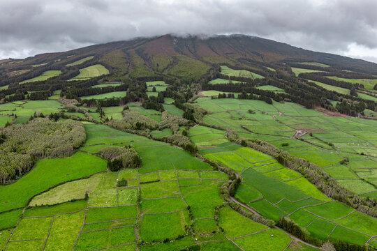 Aerial view of lush green agricultural fields and pastures divided by stone walls on the slopes of a volcanic mountain in Doze Ribeiras, Azores, Portugal.