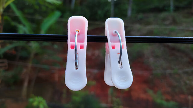Detail of a pink clothespin on a black string against a shady nature background.