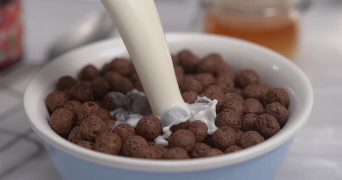 Fresh milk pouring into chocolate cereal balls bowl creating dynamic splash in ultra slow motion