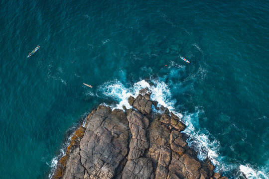 Aerial view of Lighthouse Beach with rugged rock formations jutting into the deep blue sea, featuring small traditional fishing boats navigating the coastal waters Kovalam, Kerala, India.