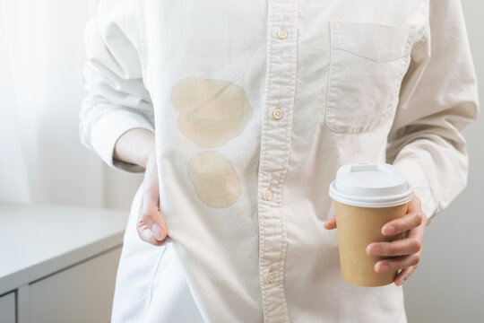 Cloth stain, disappointment asian young woman clumsy with hot coffee, tea stains on shirt, hand show making spill drop on white shirt, spot dirty or smudge on clothes at home, isolated on background