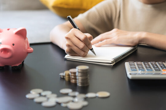 Saving money wealth concept, asian young business woman hand putting coin into piggy for saving cost, cash finance planning to spend enough money on her income for save money, payment tax, investing.