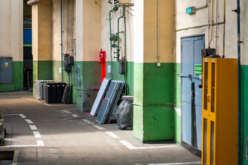 Interior of a locomotive maintenance depot with concrete floor, green and cream walls, metal doors, yellow tool cabinet, fire extinguisher, industrial pipes, and technical equipment leaning against pi © Adam
