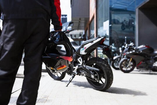 Motorcycle rider holding helmet near modern bikes outside showroom in urban lifestyle scene