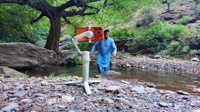a content creator stands outdoors, installing a stabilizer gimbal onto their mobile phone for smooth natural video recording