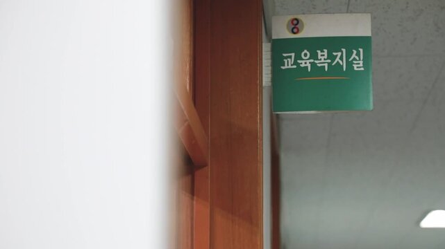 사람 스포츠 훈련 코트 야외 일상 소품 디테일 자재: 실내 복도 문틀 상단에 부착된 초록색 교육복지실 안내 표지판 문패의 한글 텍스트와 외관 디테일을 비스듬한 측면 시선으로 포착한 전경 동영상 클립입니다.
