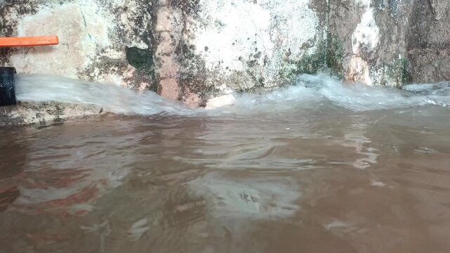 Close-up of clean water flowing from a pipe into a tank with a human hand touching the stream, water scarcity and irrigation concept