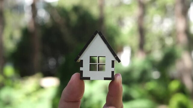 Fingers holding house model outdoors on green background. Construction, home Insurance and real estate investment. Mortgage, home loan concept